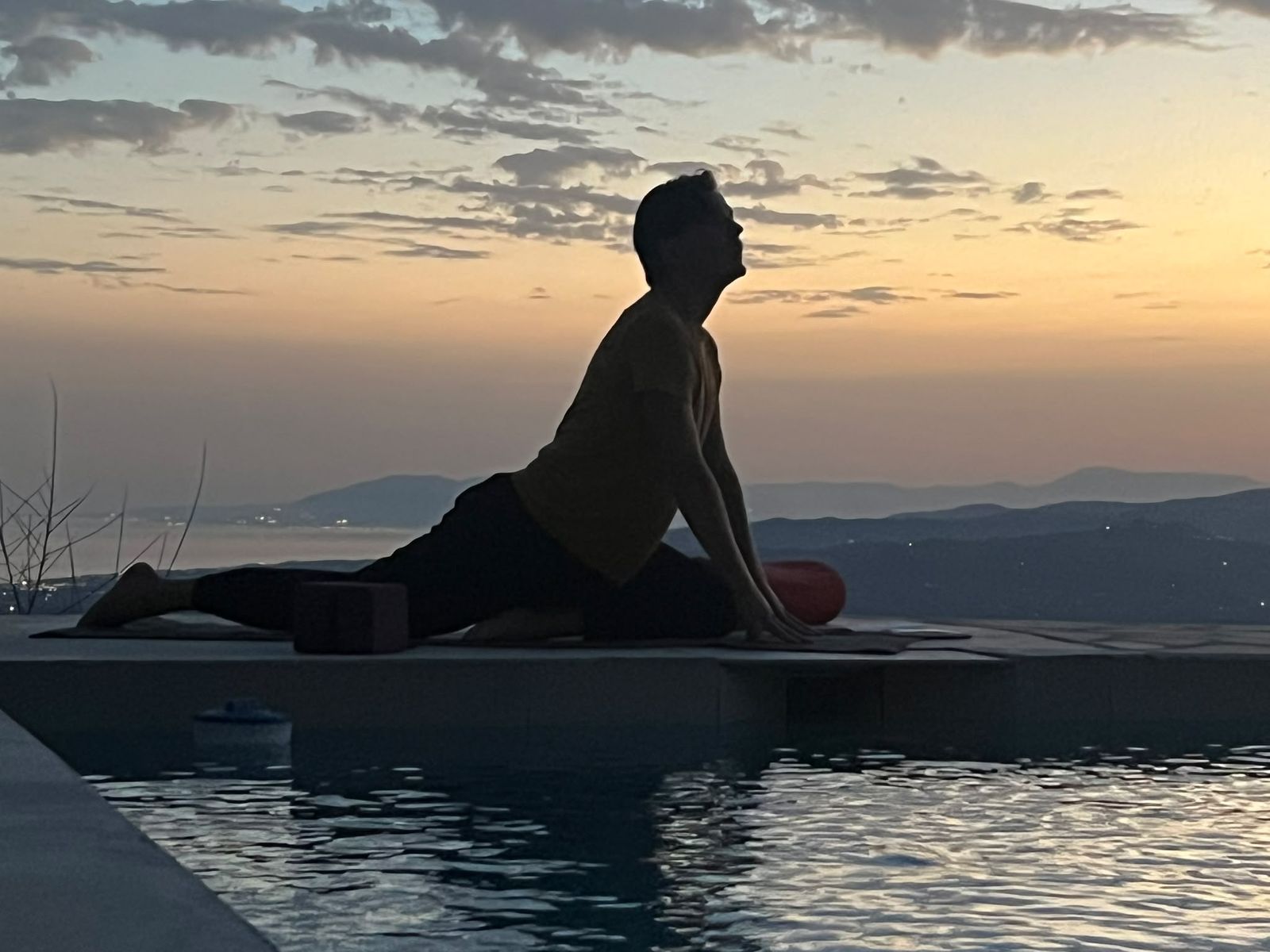 Silhouet van Kylian in een yinhouding bij zonsondergang boven een zwembad
